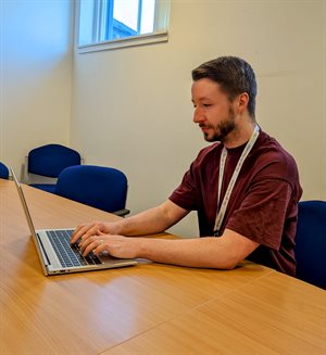 Dale is sitting at a desk working on his laptop