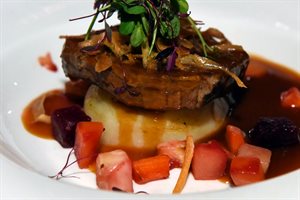 White plate with a display of food stack on top of each other such as carrots, mashed potatoes, steak, vegetables and a sauce