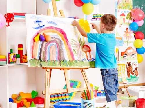 Young child creating a picture of a rainbow in nursery school