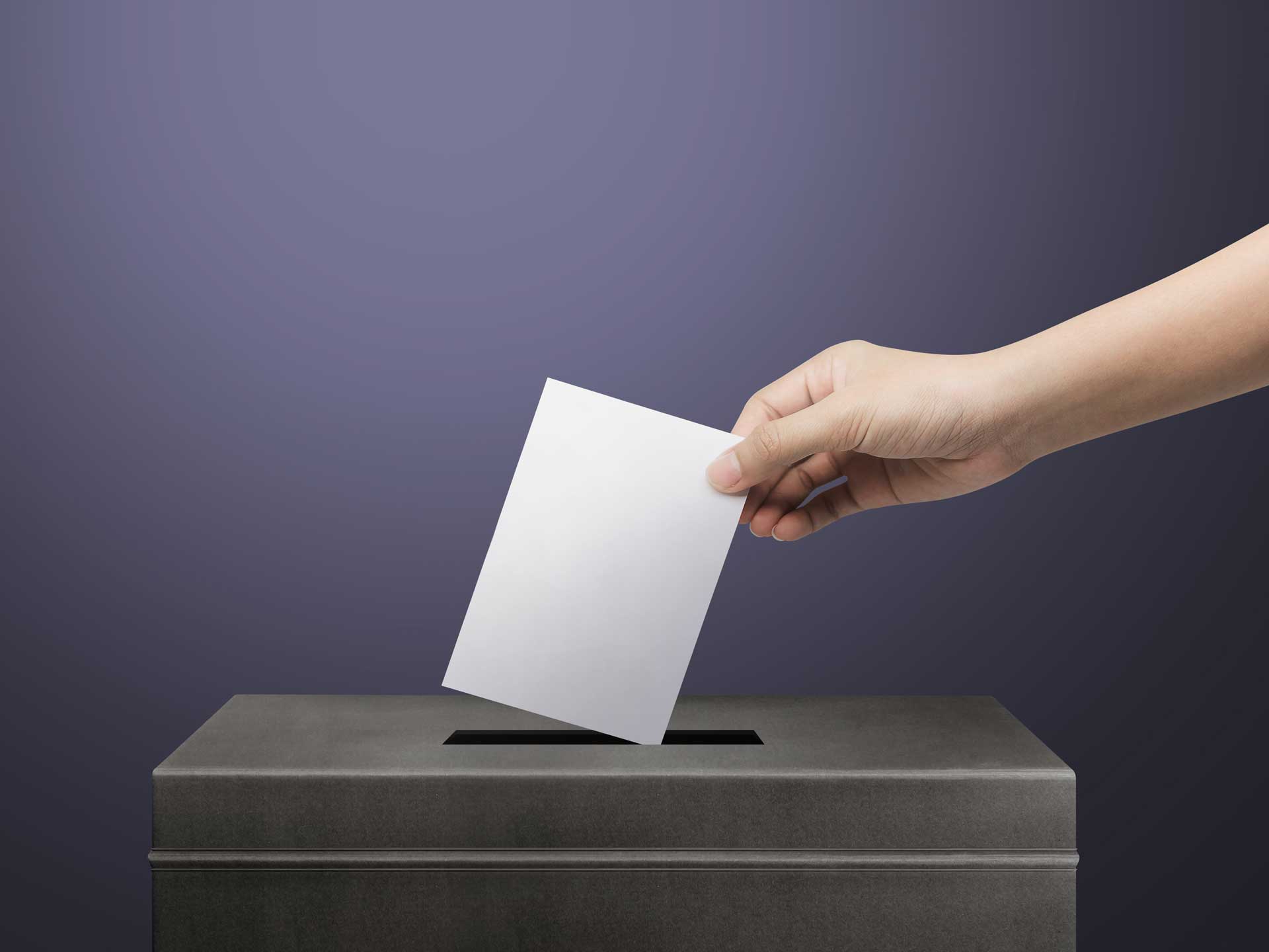 A hand inserting a ballot paper into a ballot box