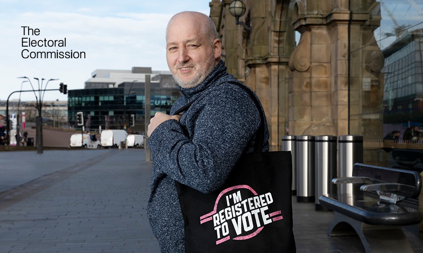 A man standing in the street holding a bag that says I'm registered to vote