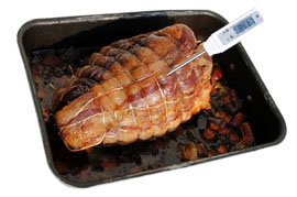 Cooked meat joint in an oven tray being tested with a food temperature probe to make sure it's cooked and safe to eat