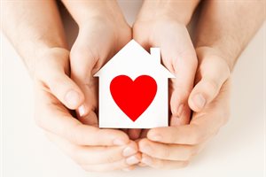 Adult and child cupping hands holding a tiny white wooden house with a red heart