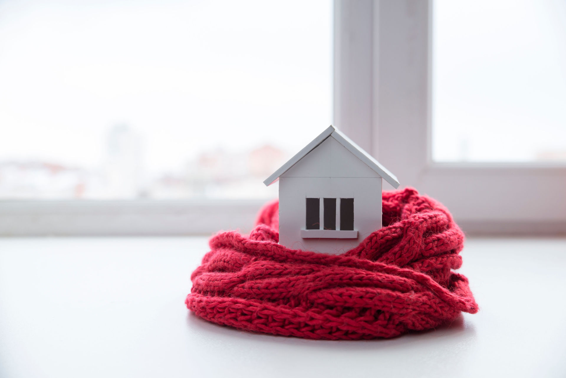 A model wooden house partially wrapped in a red scarf