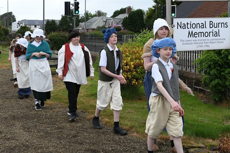 Children from Mauchline Primary School walking along a path dressed up for the Rabbie Road project