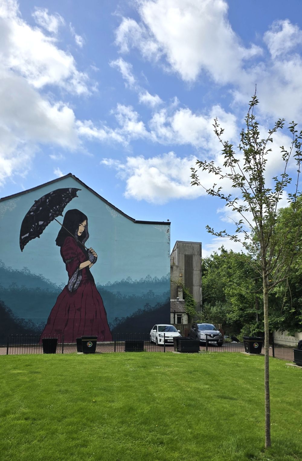 Mural of a grieving lady walking in a park carrying a black lace umbrella