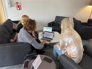 Three people sitting around a laptop at a recruitment event, demonstrating what kind work the team does