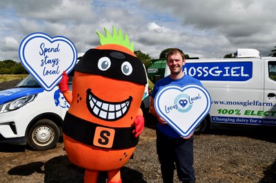 Person dressed up in an orange and black costume representing an Ayrshire Potato, named Super Tattie, standing with Farmer Bryce from Mossgiel farm