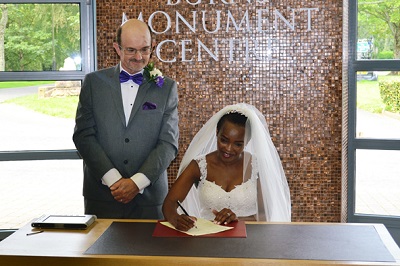 Bride sitting and groom standing at a table, smiling, at the Burns Monument Centre