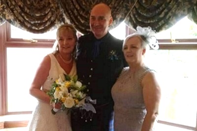 Bride and groom smiling, standing beside a guest