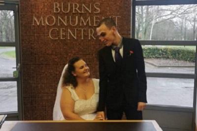 Bride sitting and groom standing at a table, smiling, at the Burns Monument Centre