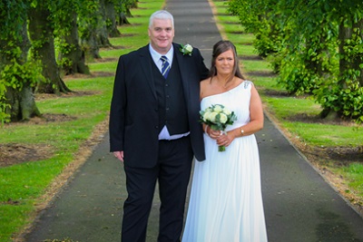 Bride and groom smiling, standing in an avenue of trees