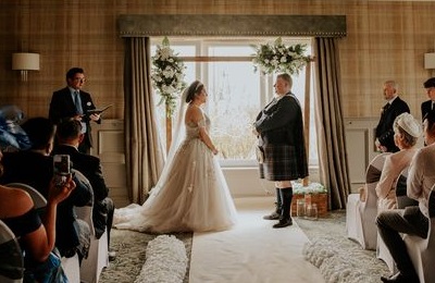 Bride and groom standing side on in front of a window, facing each other, with guests watching the marriage ceremony