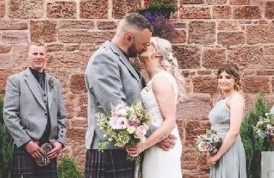 Bride and groom kissing with two guests at the back smiling