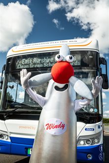 windy the windmill mascot standing in front of an electric powered bus